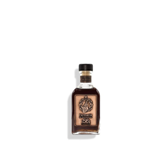 A small glass bottle of Calzolai DIFFUSER – Farmacia by Farmacia SS. Annunziata 1561 contains dark liquid, has a black cap, and features an ornate beige label. Elegant black diffuser sticks accompany it, displayed on a plain white background.