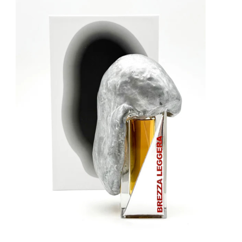 A bottle of BREZZA LEGGERA "light breeze" Eau de Parfum by Filippo Sorcinelli, filled with amber liquid and topped with an abstract silver cap, stands before white packaging with a bold black shape referencing Mediterranean notes.