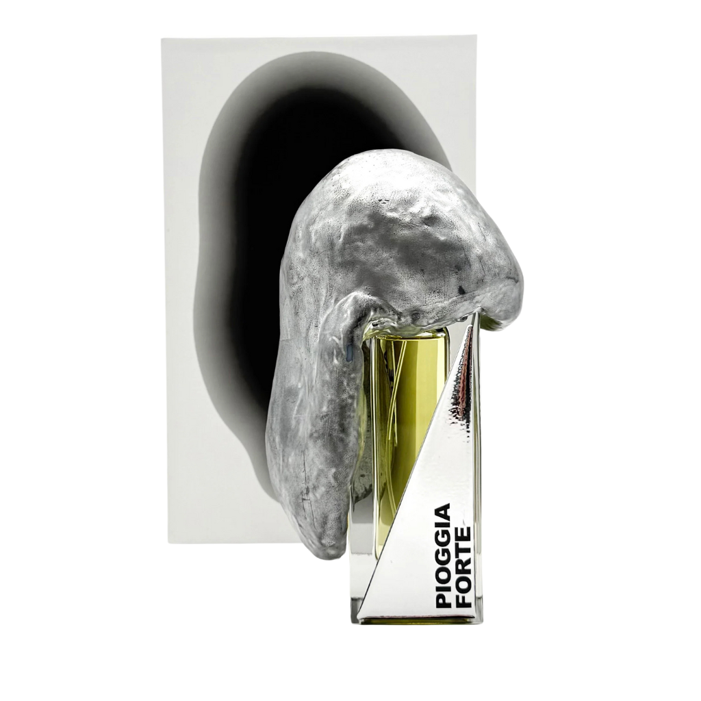 A PIOGGIA FORTE "heavy rain" Eau de Parfum by Filippo Sorcinelli sits partially obscured by an abstract silver organic-shaped sculpture, casting a shadow on the white background behind it.