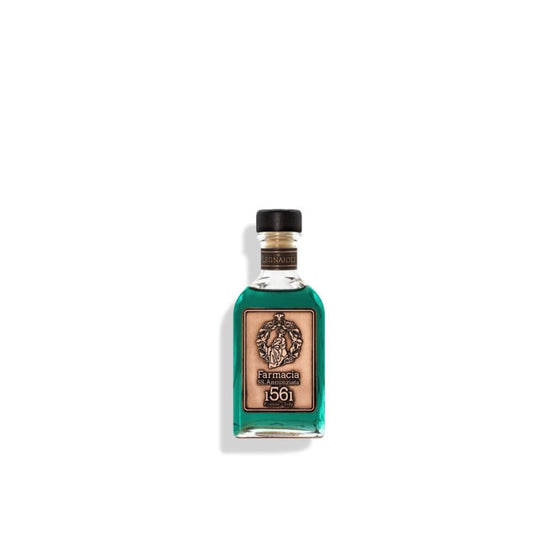 A small glass Legnaioli DIFFUSER - Farmacia by Farmacia SS. Annunziata 1561 holds teal liquid, features a black cap, tan label with emblem, and comes with black fragrance sticks, all set against a plain white background.