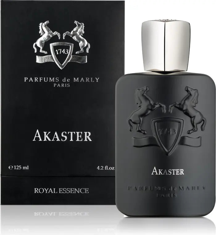 A matte black bottle of Akaster Eau de Parfum by Parfums de Marly stands next to its matching box, both adorned with silver horse emblems, elegant text, a silver cap, and labeled “Royal Essence” and “Paris.”.