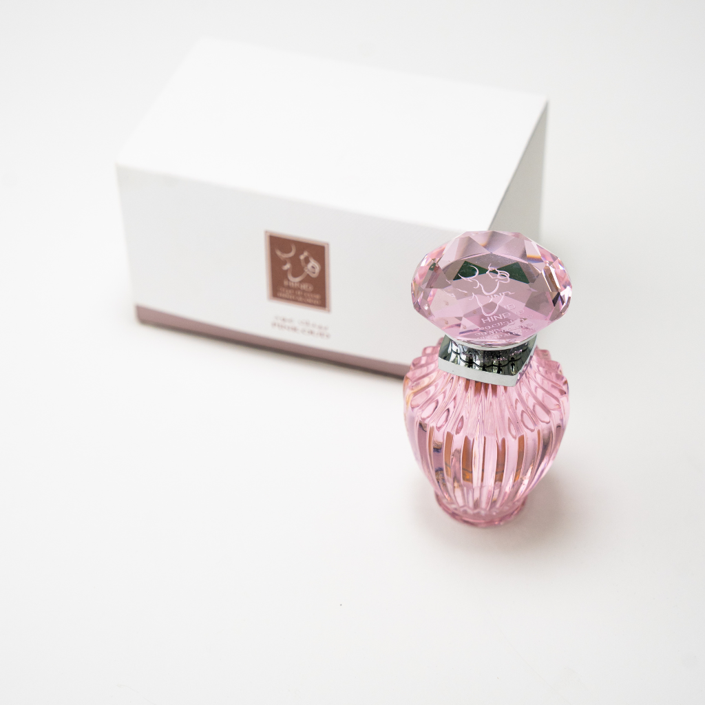 The Hind Al Oud Pink Oud Concentrated Oil 6ml features a pink faceted glass bottle with a jeweled cap, displayed before a white box with brown and white labeling—suggesting notes of jasmine and cashmere wood.