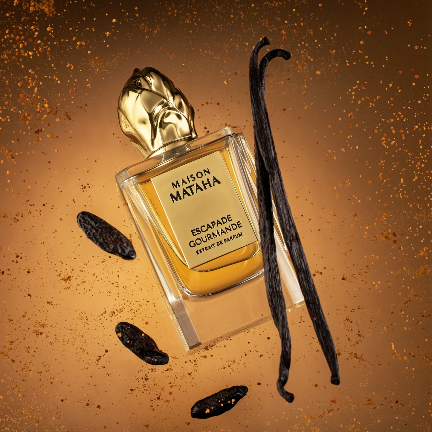 The Escapade Gourmande Extrait de Parfum by Maison Mataha, featuring a golden cap, is displayed among vanilla and tonka beans, radiating a decadent crème brûlée scent on an amber background with sparkling accents.
