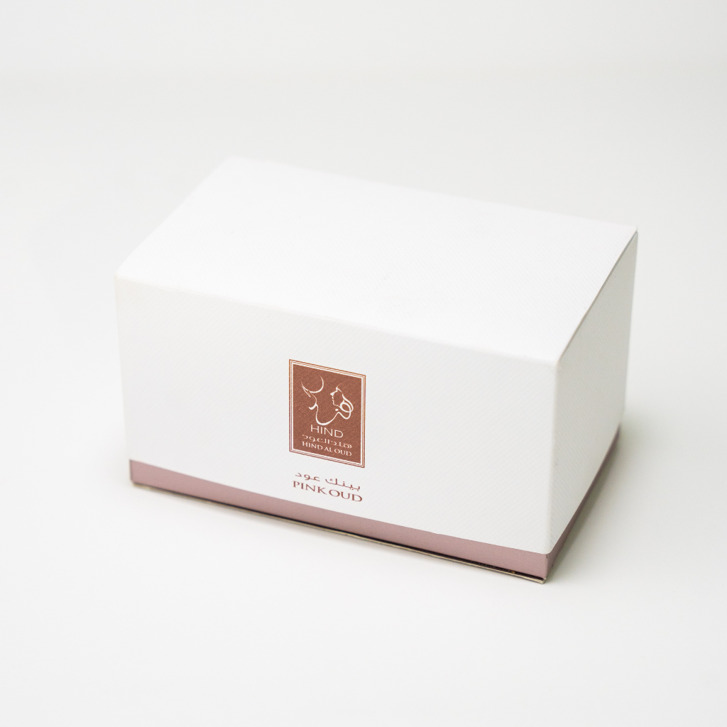 A white rectangular box with a light pink base and a brown label features Hind Al Oud branding and the product name Pink Oud Concentrated Oil 6ml in English and Arabic, evoking Cashmere Wood and Agarwood notes.