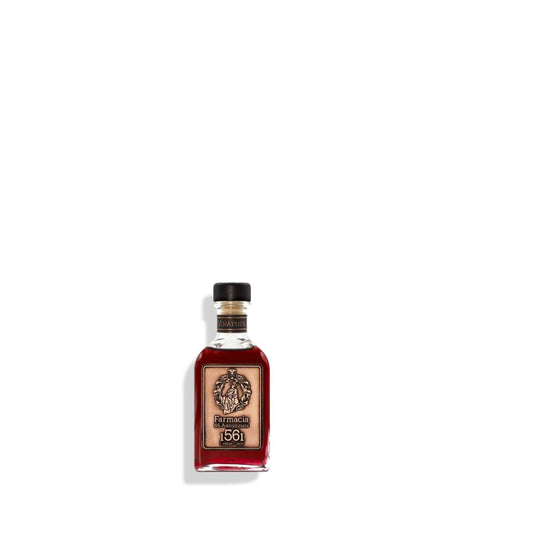 A small glass Vinattieri DIFFUSER by Farmacia SS. Annunziata 1561, filled with dark red liquid, a black cap, and detailed label, recalls Arte dei Vinattieri and exudes a subtle fruity wine scent against a white background.