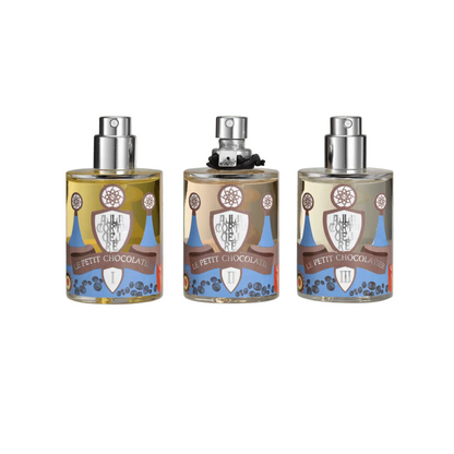 Three Le Petit Chocolatier - Nobile 1942 spray bottles by Nobile 1942, with colorful chocolate-inspired designs, are shown on a white background. The center bottle features a black accessory around its neck.