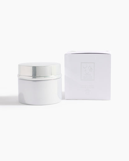 A white cosmetic jar with a shiny silver lid sits beside a matching white box with Hind Al Oud branding, set against a plain backdrop—showcasing Pink Smoke Dokhoon by Hind Al Oud, inspired by jasmine and pink oud.