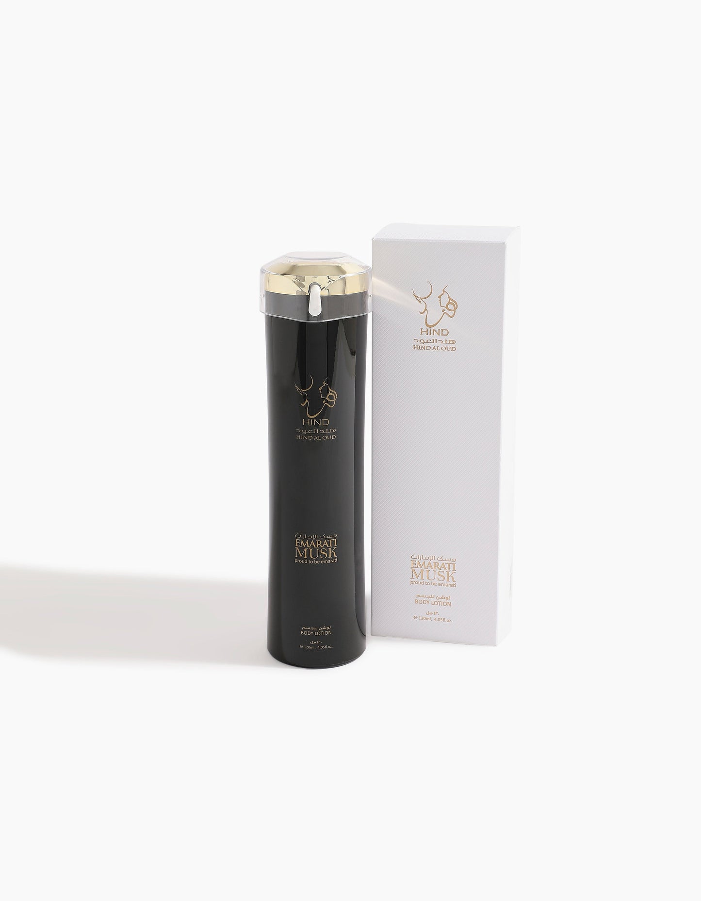 A tall black bottle of Emarati Musk Body Lotion by Hind Al Oud, featuring a metallic gold cap and branding, stands next to a matching white box with gold text. The luxurious scent blends notes like Dates and Vanilla.