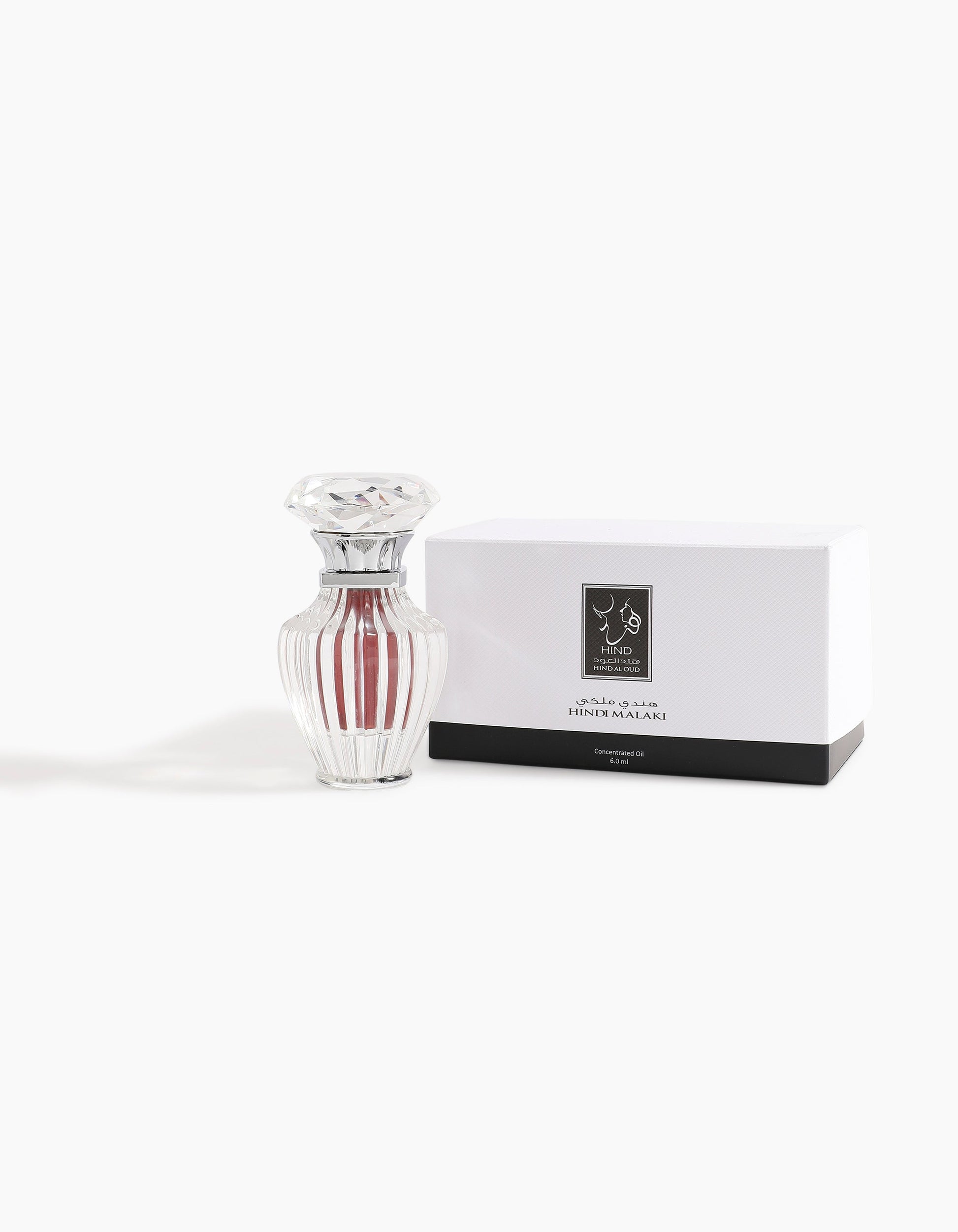 A clear, ribbed glass bottle with a faceted lid sits beside a white box in black and silver, both labeled in Arabic and English. The box displays Hind Al Oud's Hindi Malaki Pure Dehn Oud Concentrated Oil 6ml—a refined agarwood scent.