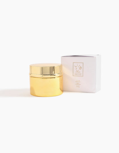 A gold Hind Dokhoon jar with a shiny lid is shown beside a white box featuring the minimalist gold Hind Al Oud logo and text, set against a plain white background.