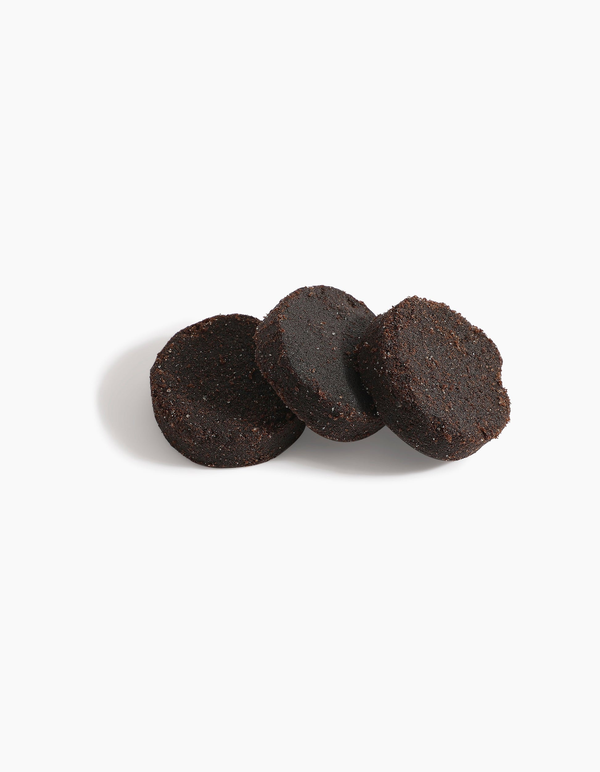 Three round, dark brown Hind Dokhoon - Hind Al Oud pucks by Hind Al Oud are arranged on a white background, with one puck leaning against the others and a soft shadow cast to the left.
