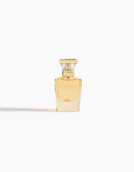 Ahojas Hair Mist by Hind Al Oud is displayed in a clear glass bottle with golden liquid and a gold-silver rectangular cap, set against a plain white background with a soft shadow on the left.