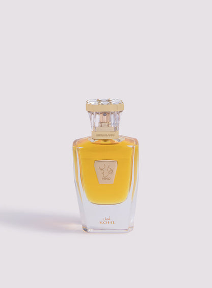 The clear glass bottle of Kohl Parfum by Hind Al Oud showcases golden-yellow liquid, with a gold cap and label featuring Arabic and English text, reflecting an elegant fragrance infused with luxurious saffron notes against a light background.