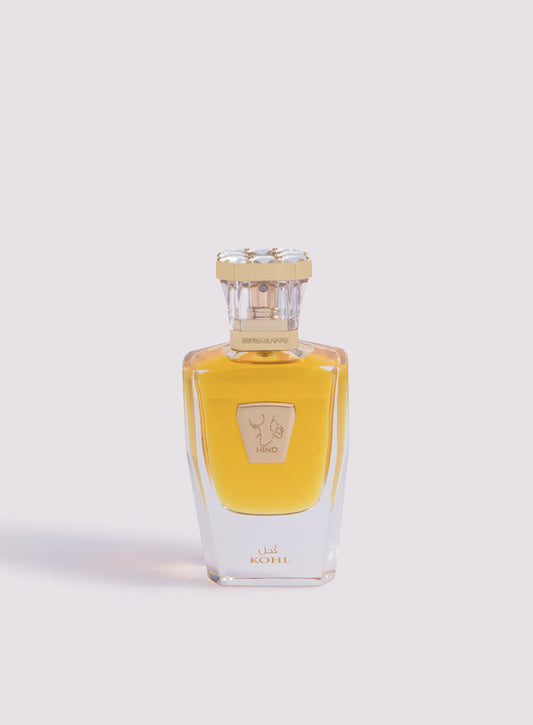 The clear glass bottle of Kohl Parfum by Hind Al Oud showcases golden-yellow liquid, with a gold cap and label featuring Arabic and English text, reflecting an elegant fragrance infused with luxurious saffron notes against a light background.