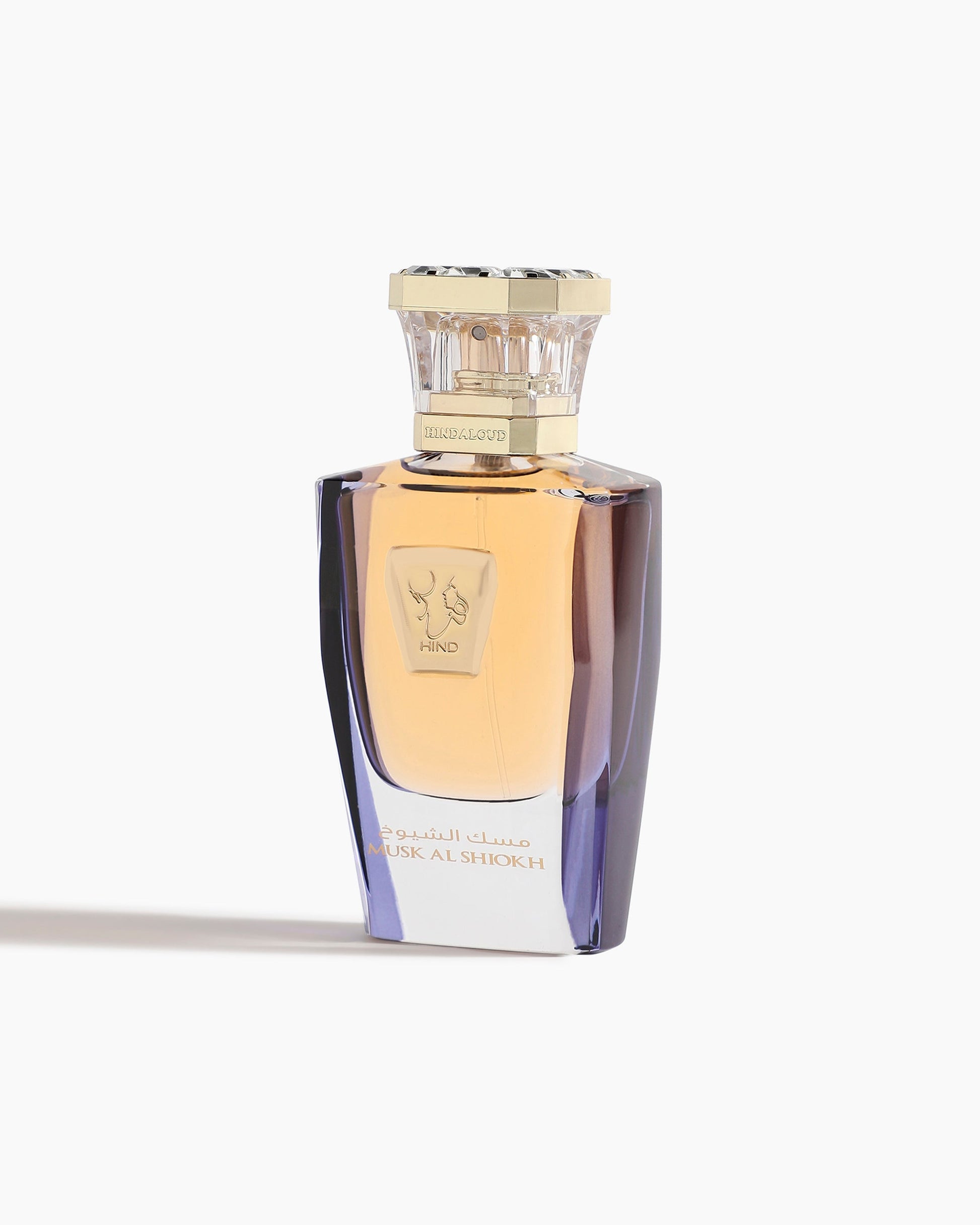 The luxurious Musk Al Shiokh Parfum by Hind Al Oud comes in an amber-hued glass bottle with a gold cap, featuring gold accents, Arabic script, and the brand logo—showcasing Emarati heritage against a white background.