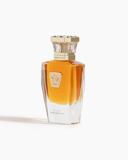 A clear glass Sheikh A Parfum by Hind Al Oud features golden liquid, a decorative gold cap, and a gold emblem. Inspired by Hind Al Oud, the label at the base displays SHEIKHA in English and Arabic.