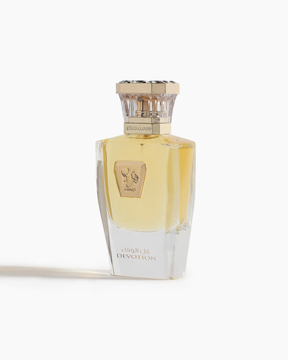 Devotion Parfum by Hind Al Oud is an elegant oriental perfume in a clear glass bottle with a gold cap, golden liquid, and an Arabic "DEVOTION" label. The white design features two hands forming a heart shape.