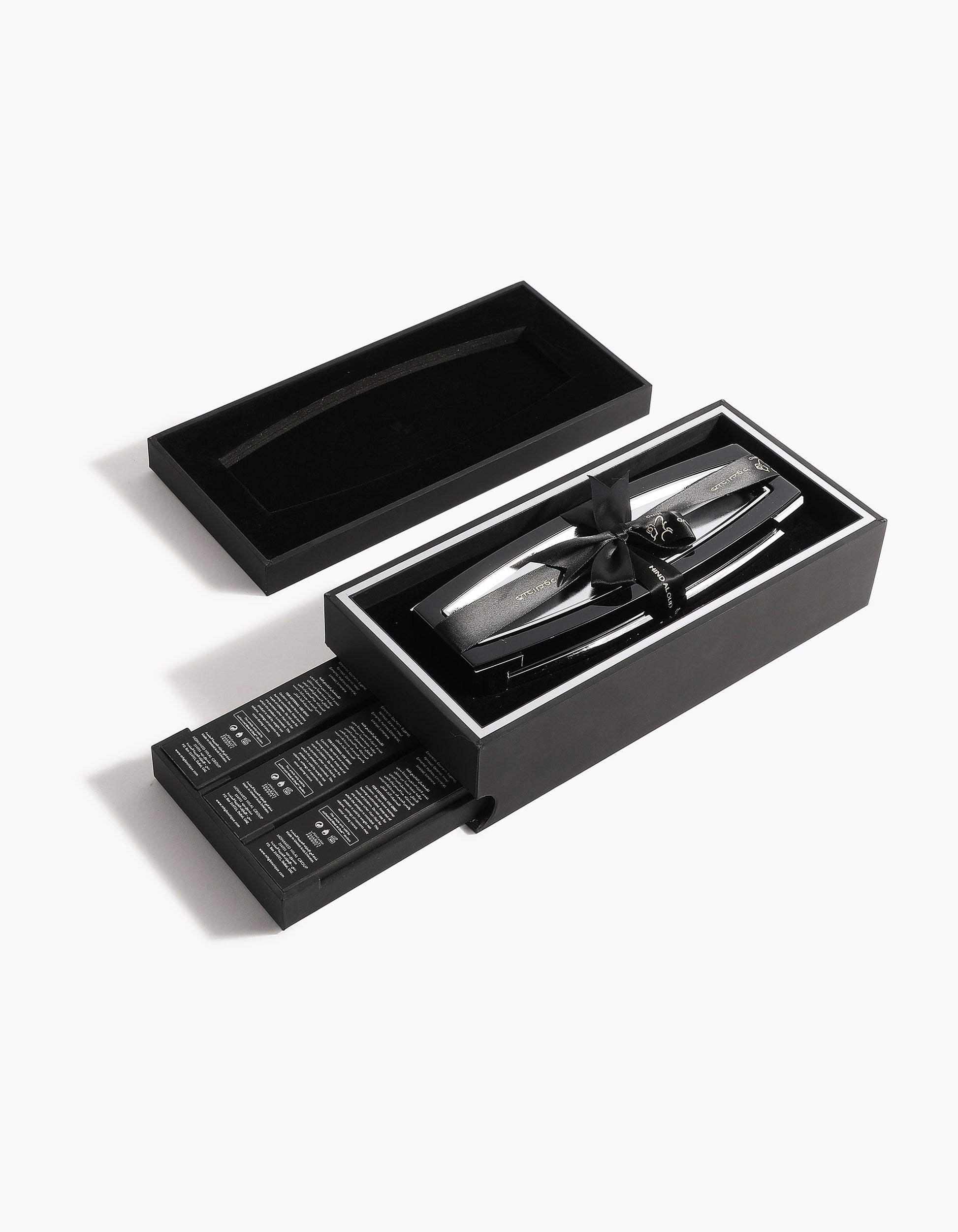 The Oud Obsession Gift Set by Hind Al Oud features a sleek black box with a sliding drawer containing several grooming products and a metallic hair clipper, arranged neatly on a white background.
