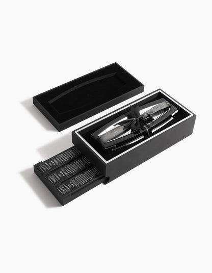 The Oud Obsession Gift Set by Hind Al Oud features a sleek black box with a sliding drawer containing several grooming products and a metallic hair clipper, arranged neatly on a white background.