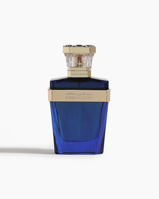 A deep blue Deep Masa'ey Parfum bottle by Hind Al Oud, adorned with gold accents and a clear faceted cap, stands out on white. The label appears in English and Arabic, hinting at notes of Hilal's Oud and warm Cashmere Wood.