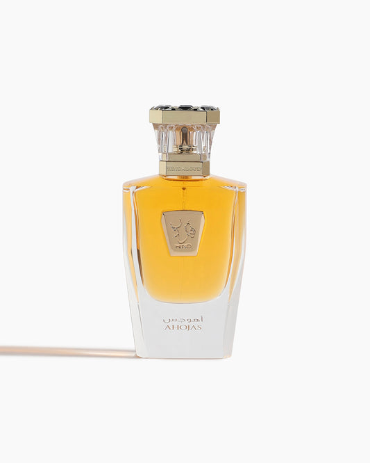 A transparent glass bottle with amber liquid, gold embossed emblem, and a gold-and-black cap. The label shows Ahojas in English and Arabic, identifying it as Ahojas Parfum by Hind Al Oud.