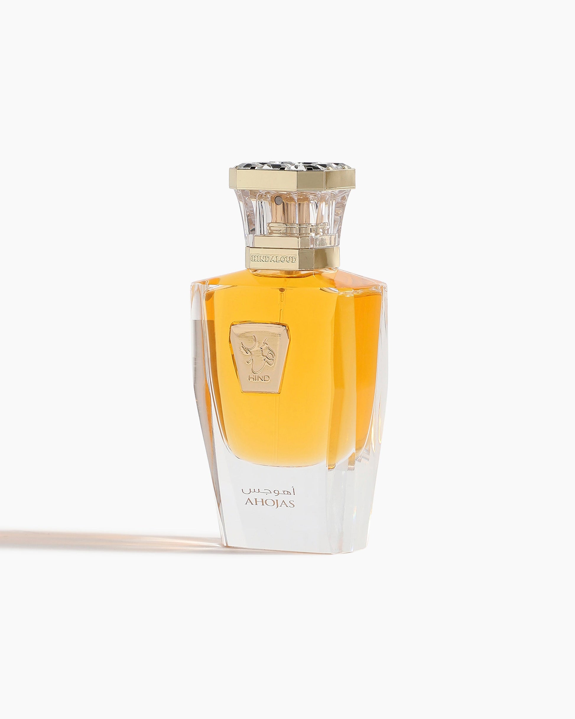 Ahojas Parfum by Hind Al Oud features a clear glass bottle with amber liquid, a gold cap, and a decorative gold label. “AHOJAS” and Arabic text adorn the front, reflecting this luxurious fragrance from Hind Al Oud.