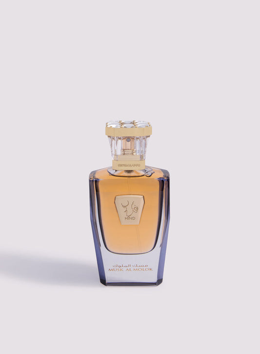 Musk Al Molok Parfum by Hind Al Oud features amber liquid in a clear glass bottle with a gold cap and label displaying Arabic and English text. This floral musk perfume is photographed against a light background.