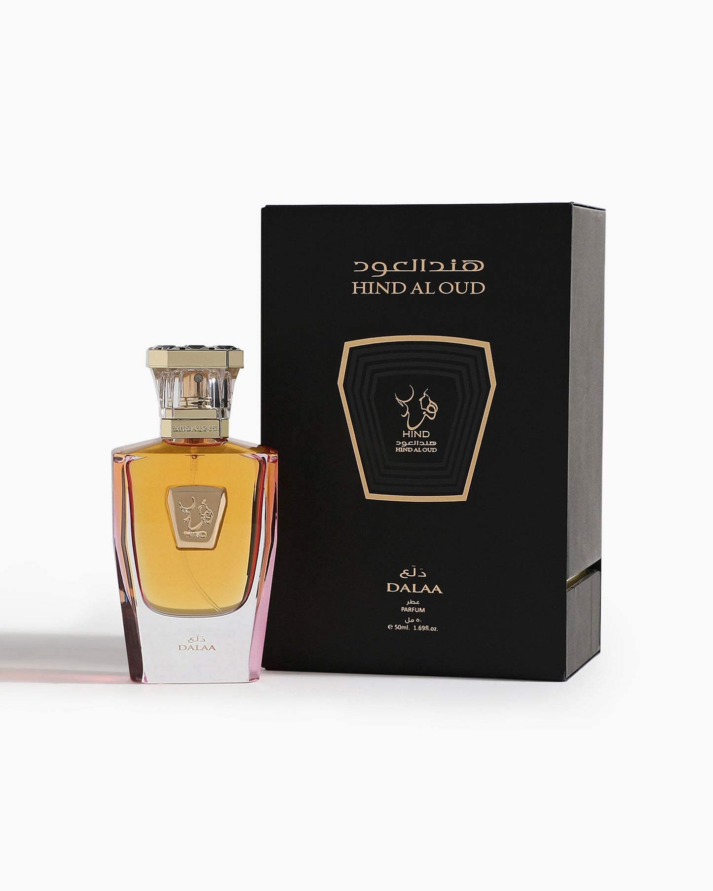 A bottle of Dalaa Parfum - Hind Al Oud by Hind Al Oud, with spicy floral notes, stands next to its black and gold box featuring Arabic and English text. The amber liquid shines beneath a stylish cap.