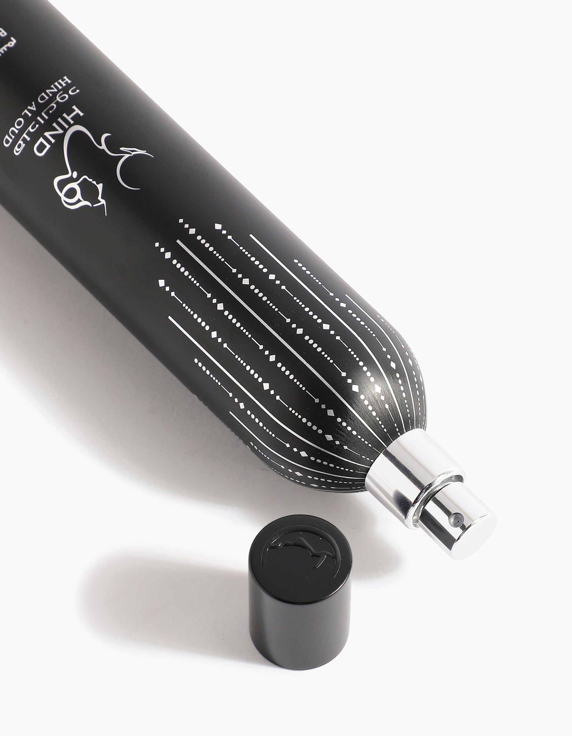 A black tube of Sheikh A Body Spray by Hind Al Oud, adorned with white dotted lines and a deer illustration, lies on its side with the cap nearby on a white surface, exuding subtle hints of spices and agarwood.