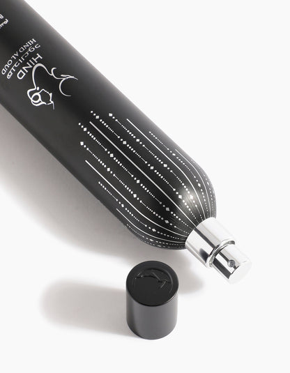 A black tube of Sheikh A Body Spray by Hind Al Oud, adorned with white dotted lines and a deer illustration, lies on its side with the cap nearby on a white surface, exuding subtle hints of spices and agarwood.