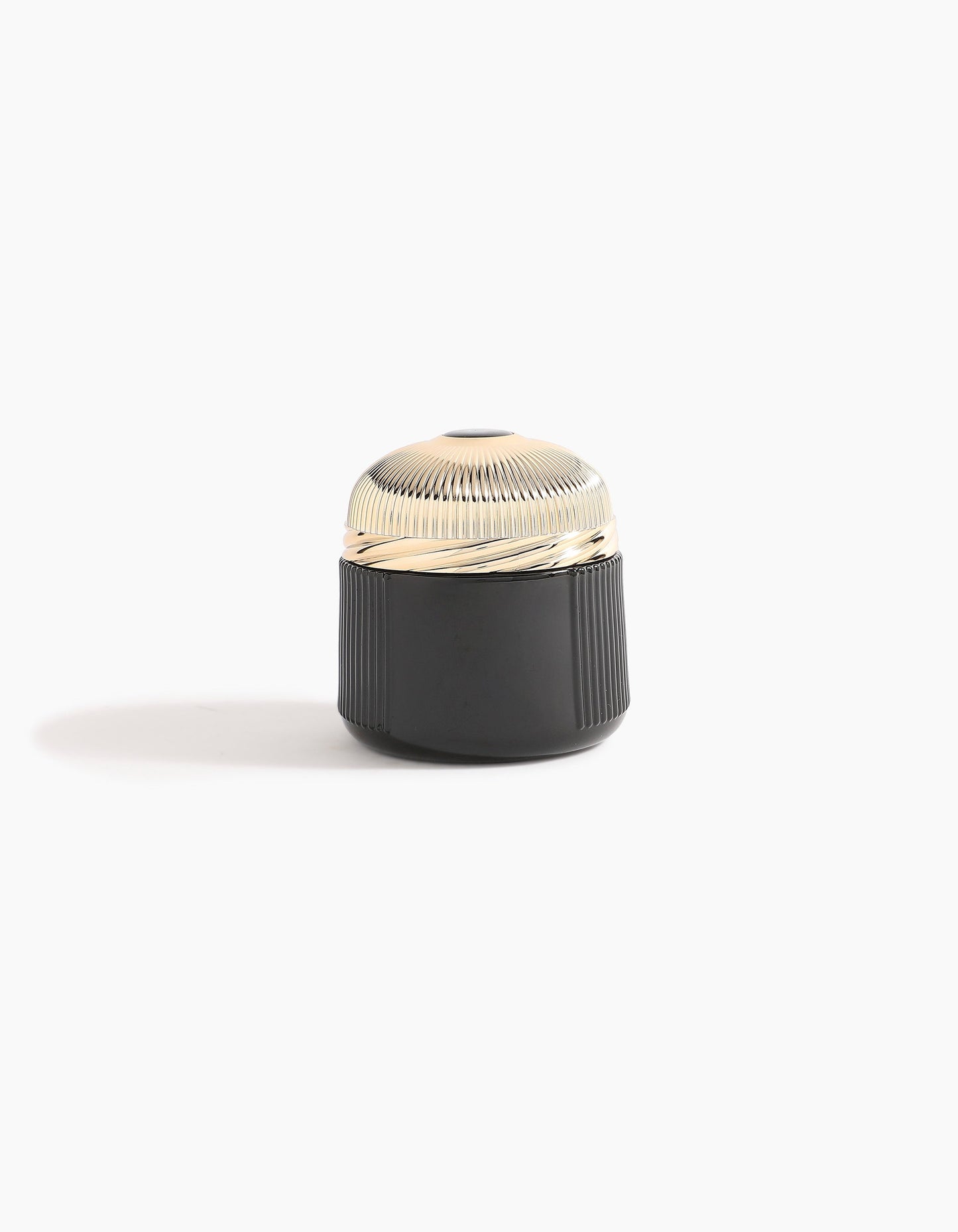 A small, round container with a ribbed, shiny gold lid and a black, textured base—echoing Agarwood luxury—Sheikh A Oud Mubakhar by Hind Al Oud rests on a plain white background with a soft shadow to the left.