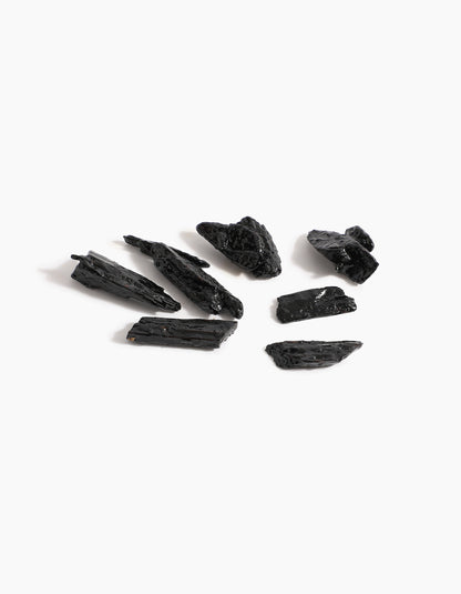 Eight pieces of rough, black tourmaline are scattered on a white surface, their jagged, shiny finish evoking the luxurious essence of Sheikh A Oud Mubakhar by Hind Al Oud.