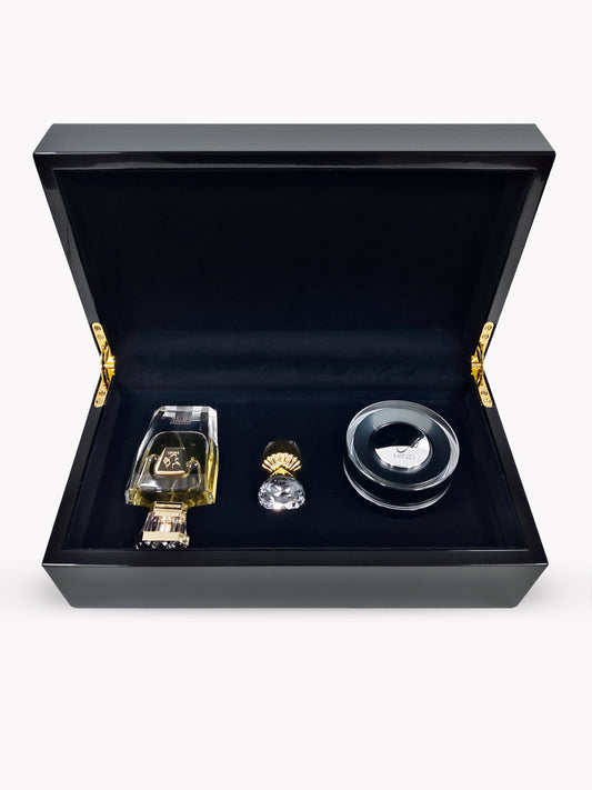 The Emarati Musk Trio Shield Edition Gift Box by Hind Al Oud features a black velvet-lined box with gold hinges, containing a perfume bottle, crystal stopper, and round container arranged neatly inside.