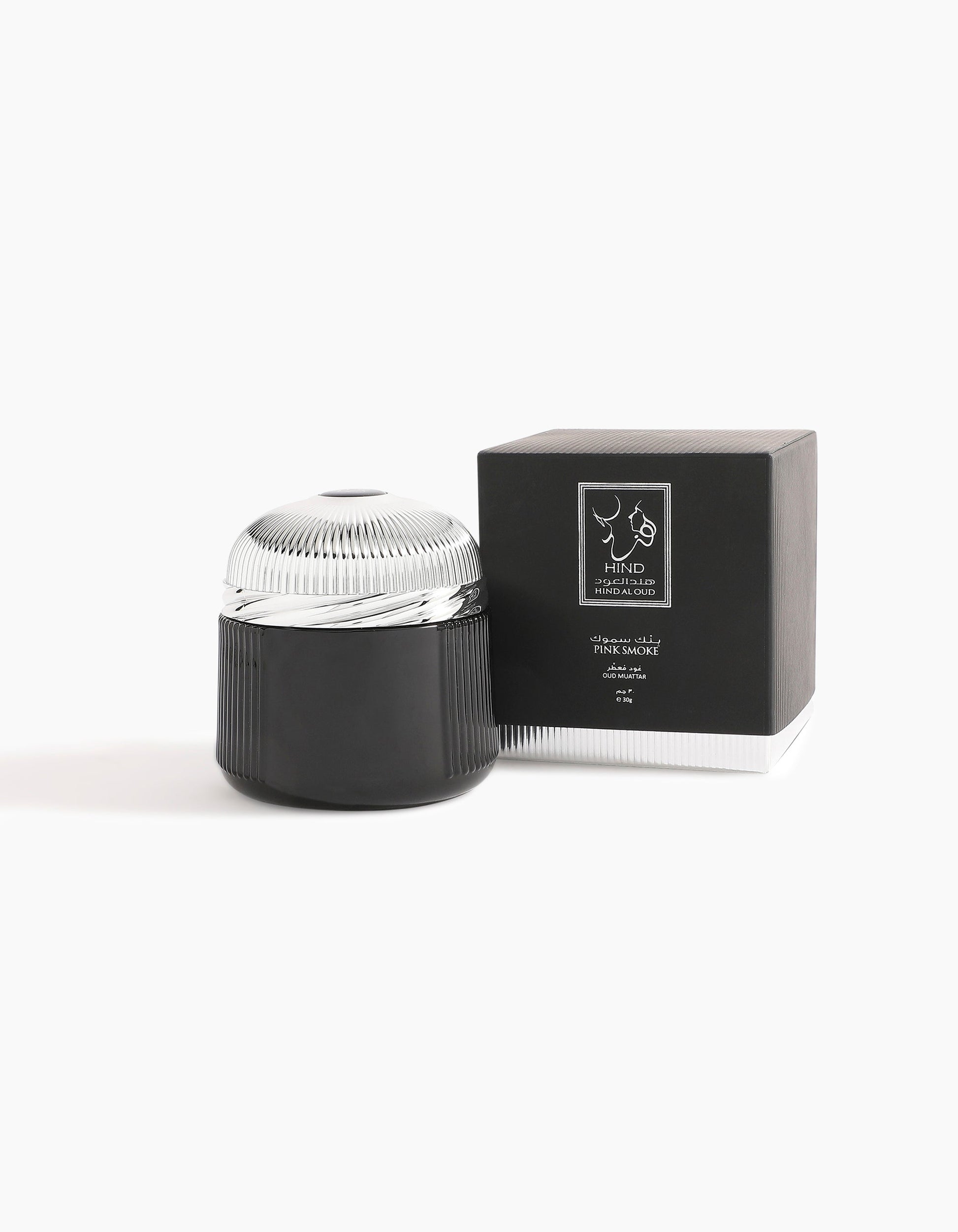 A black and silver cosmetic jar with a ridged lid sits next to a matching black box featuring a white label and the Hind Al Oud logo, evoking the refined notes of Pink Smoke Oud Muattar, set against a plain white background.