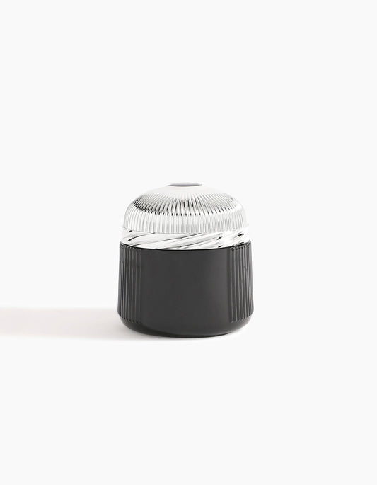 A sleek, cylindrical black container with a ribbed texture and metallic ridged lid, showcased on a white background—reflecting the luxury of Hind Al Oud’s Oud Al Qasr Oud Muattar and its signature woody scent.