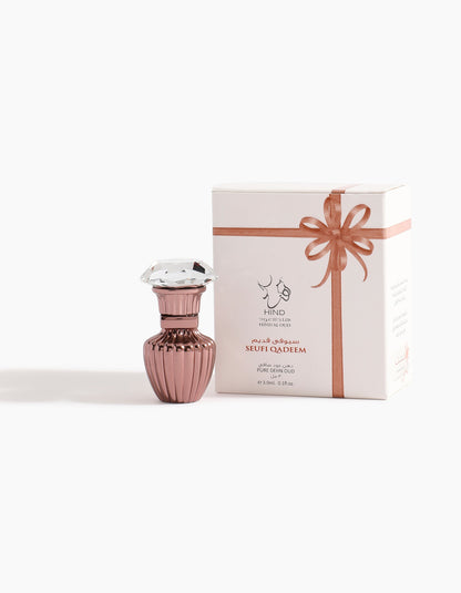 A decorative pink bottle with a faceted cap stands next to a white box tied with a pink ribbon, labeled Hind Al Oud Seufi Qadeem Petite Concentrated Oil 3ml—an Emirati treasure crafted from luxurious oud.