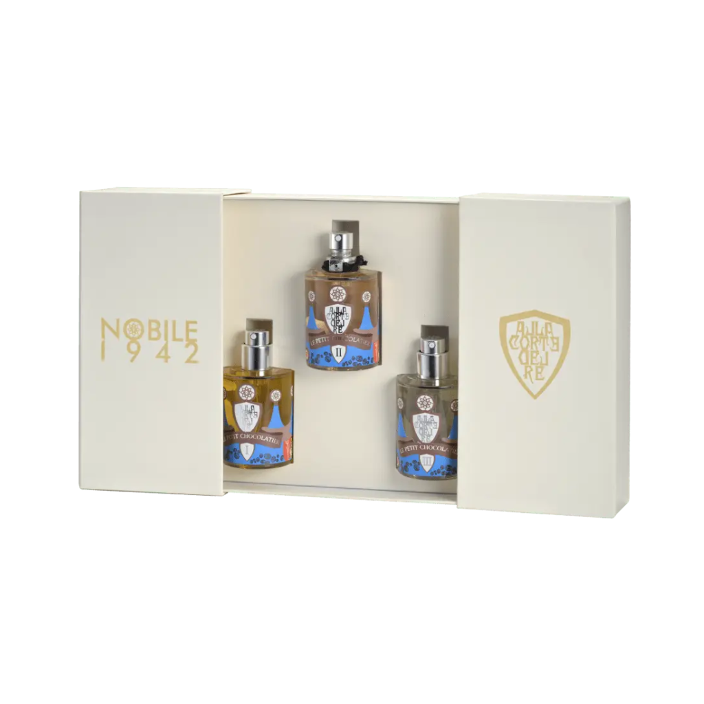 The cream-colored Le Petit Chocolatier - Nobile 1942 box set by Nobile 1942 features gold lettering and three detailed perfume bottles with silver caps, beautifully displayed in an open-sided box for this chocolate-inspired fragrance trio.