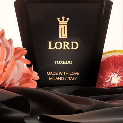 A black LORD MILANO TUXEDO Eau de Parfum bottle with a crown logo is shown among a pink flower, grapefruit slice, and black satin—an elegant luxury fragrance for men and women.