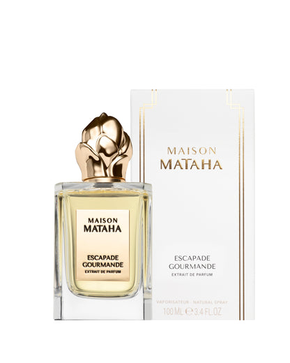 The 100 mL Escapade Gourmande Extrait de Parfum by Maison Mataha features a vanilla fragrance reminiscent of crème brûlée, presented in a bottle with a gold floral cap and displayed before its white and gold packaging.