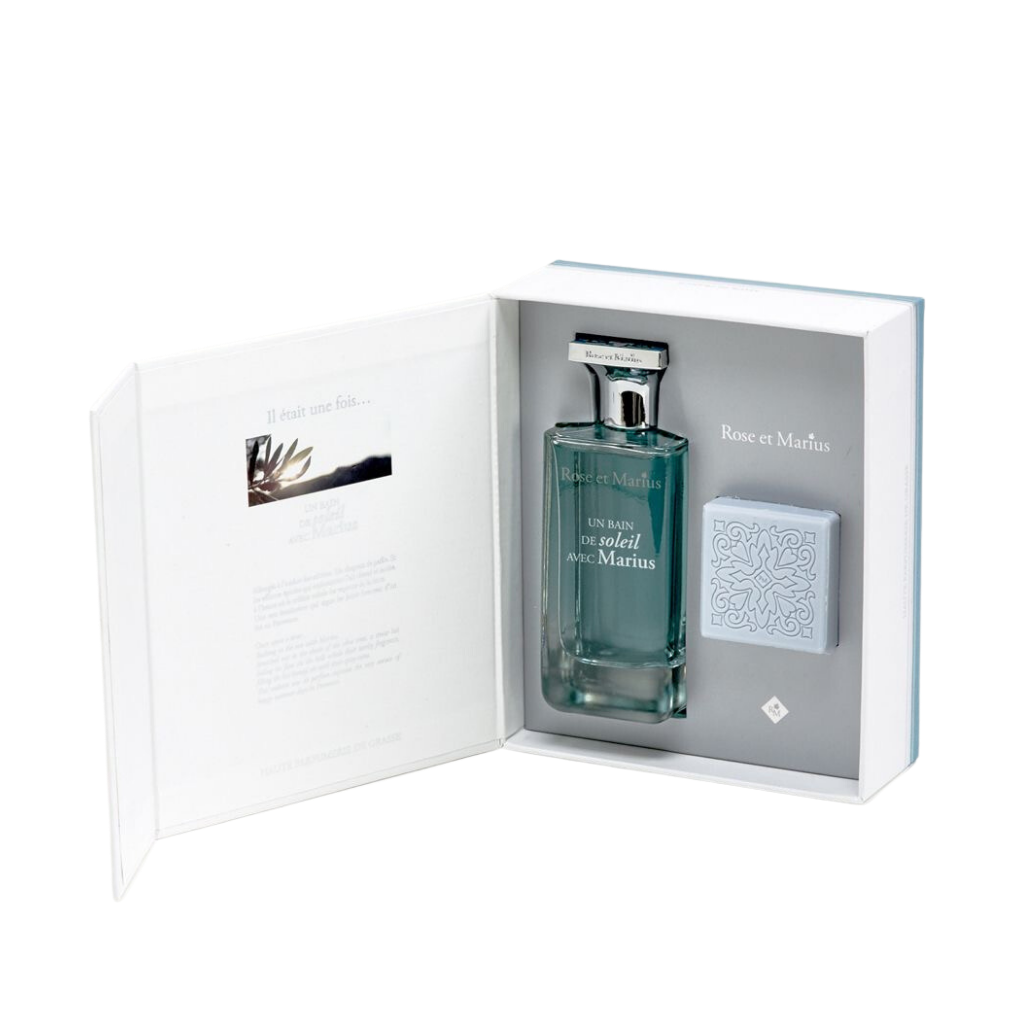 The GIFT SET BASKING IN THE SUN WITH MARIUS by Rose Et Marius includes a perfume and patterned light blue soap, elegantly presented in an open book-style box with inner text and image, capturing the essence of fine Grasse fragrance.