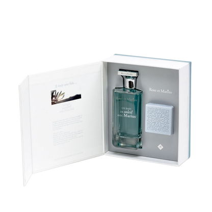 The GIFT SET BASKING IN THE SUN WITH MARIUS by Rose Et Marius includes a perfume and patterned light blue soap, elegantly presented in an open book-style box with inner text and image, capturing the essence of fine Grasse fragrance.