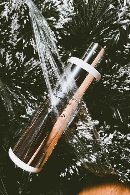 A shiny 250 ml SUPERFLUO ASCETIC VANILLA SHOWER GEL by Filippo Sorcinelli, wrapped in plastic, rests on snow-dusted pine branches for a festive and elegant display.