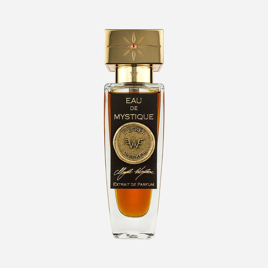 A clear glass Wesker Eau De Mystique Eau de Parfum bottle, filled with amber liquid, features a black label with a gold medallion, the Wesker logo, hints of Sicilian Blood Oranges, and a gold cap topped with a decorative star.