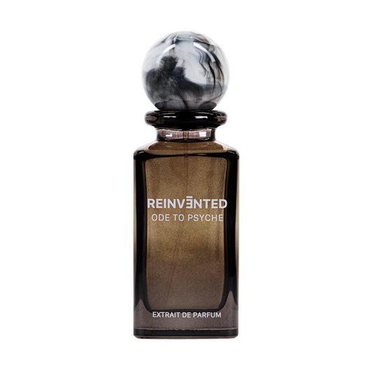 A dark glass bottle of REINVĒNTED’s ODE TO PSYCHE Extrait de Parfum – REINVENTED features a round marbled black-and-white cap and “EXTRAIT DE PARFUM” at the base, reflecting its rich oriental woody scent.