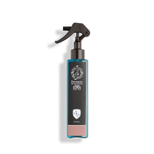 A rectangular blue Fabbri Room Spray bottle by Farmacia SS. Annunziata 1561 features a black trigger nozzle, white emblem, and a small scissors icon at the bottom.
