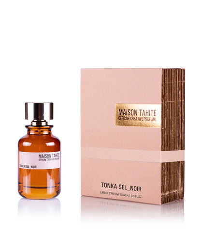 A 100ml amber bottle of Maison Tahite Tonka Sel Noir Eau de Parfum rests by its beige and gold box. The sensual fragrance combines rich tonka bean with alluring Black Salt, showcased in a sleek design with a black cap and white label.