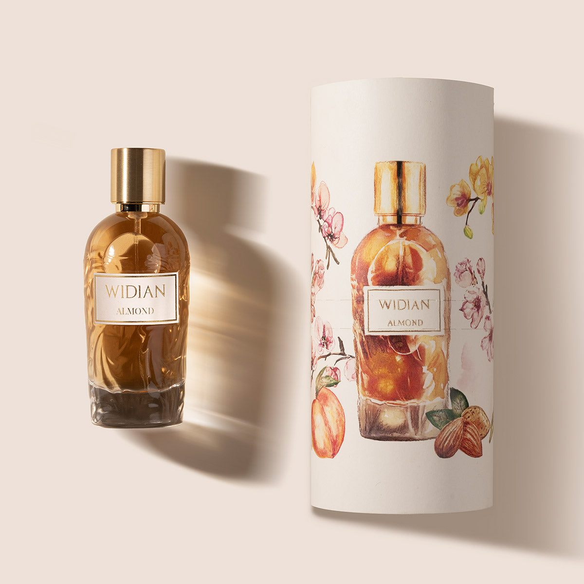 A glass bottle of Almond Eau de Parfum by Fragrapedia Haus, with a gold cap, stands beside its cylindrical packaging adorned with floral and almond designs on a light background, reflecting the creamy, rich oriental scent inside.