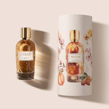A glass bottle of Almond Eau de Parfum by Fragrapedia Haus, with a gold cap, stands beside its cylindrical packaging adorned with floral and almond designs on a light background, reflecting the creamy, rich oriental scent inside.