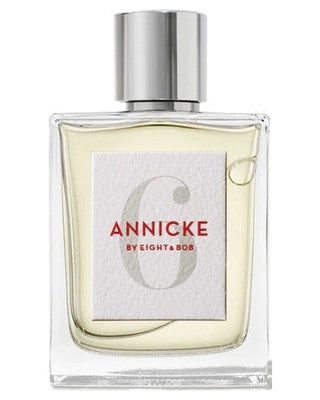A clear glass perfume bottle with a silver cap, featuring a white label that reads ANNICKE 6 BY EIGHT & BOB in red and gray text. The liquid inside is light yellow.