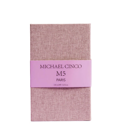 A rectangular box in textured light pink fabric with a matching band, labeled Fragrapedia Haus M5 Eau de Parfum by Michael Cinco, 100 ml e 3.4 fl.oz, hints at the luxurious and seductive scent inside.